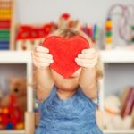 Toddler girl handing a large toy heart